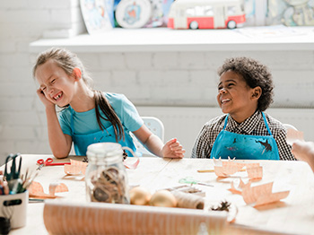 Two kids at a craft table laughing.