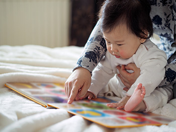 Baby looking at picture book on a bed.