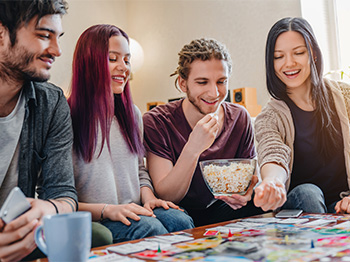 Four teens eating popcorn and playing a board game together