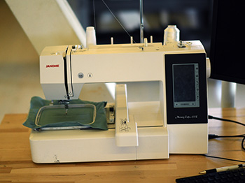 A digital embroidery machine on a wooden desk.