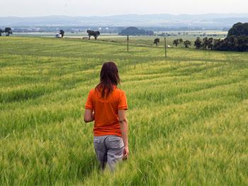 A person in an orange shirt stands in a field of tall grass looking out over the landscape