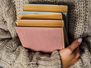 Person in wool sweater holding a stack of books.
