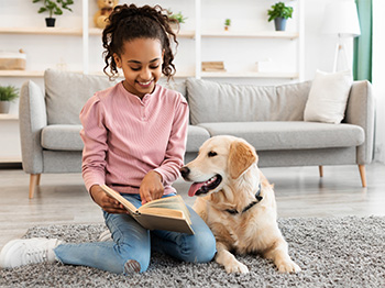 A child points at an open book and a dog looks where she points