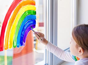 Child painting a rainbow on a window