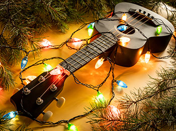 Ukulele with a string of coloured lights and evergreen boughs.