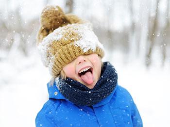 Child with touque outside in snow, catching a snowflake on their tongue.