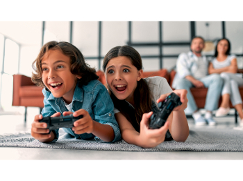 Two young people lying on the floor, playing video games, laughing.