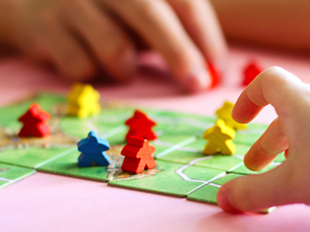 Two children are playing a board game and interacting with the colourful game pieces.