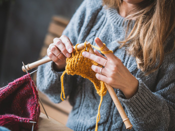 An adult knitting with thick needles and yellow thread.