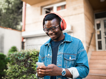 An adult wearing headphones and looking at a smartphone.