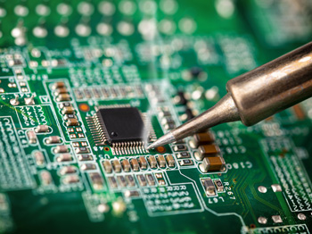 A soldering iron making contact with circuit board components.