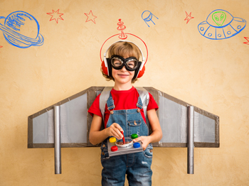 Child with spacecraft wings, goggles, and a control pad in hand smiling.