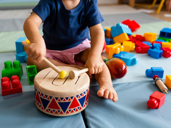A child banging a drum and sitting on the floor.