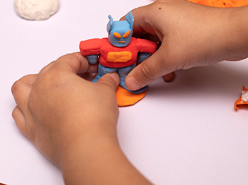 Child's hands making a clay robot on a table.