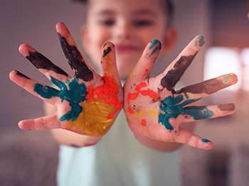 A toddler holding up both hands that are painted like rainbows.