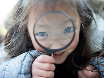 Child looking through a magnifying glass with magnified eyes.