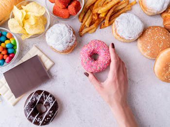 A hand holding a donut surrounded by unhealthy food.