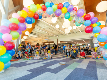 A group of families in a library with an arc of colourful balloons above.