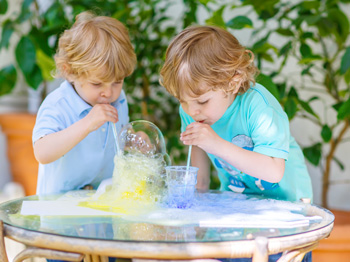 Two happy children making experiment with colourful bubbles.