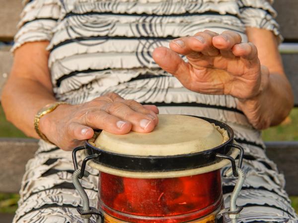 An elderly person banging their hands on a drum.