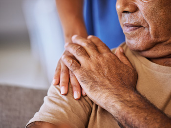 An elderly person with their hand on another on their shoulder.
