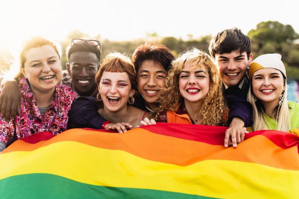 Diverse group of teens holding a large pride flag.