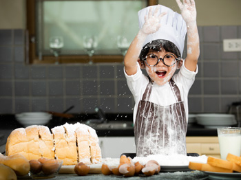 A child in a chef's uniform baking in the kitchen.