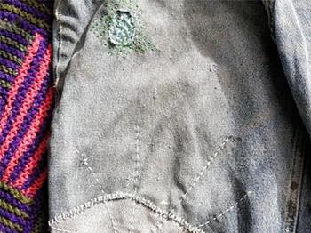 A photograph showing a pair of jeans mended with visible stiches 