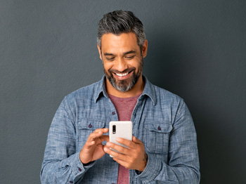 An adult smiling and looking at a smartphone in hand.