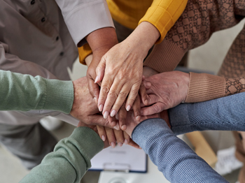 A group of older adults touching hands in a circle.
