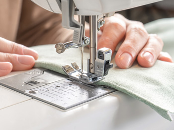 Hands holding down fabric as it passes through a sewing machine.