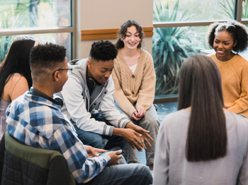 A group of teenagers talking in a seated circle.