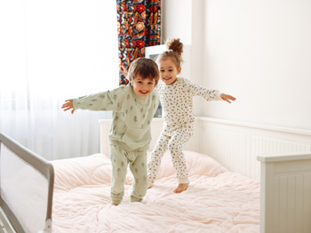 Happy children in pyjamas jumping on a bed.