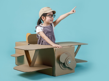 A child sitting in a cardboard airplane with their arm extended forward.