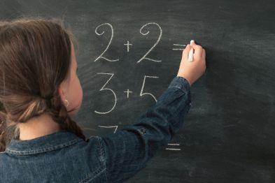 Child in front of a blackboard completing math problems.