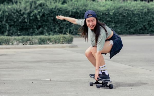 A skateboarder crouches as grabs her deck as she rides